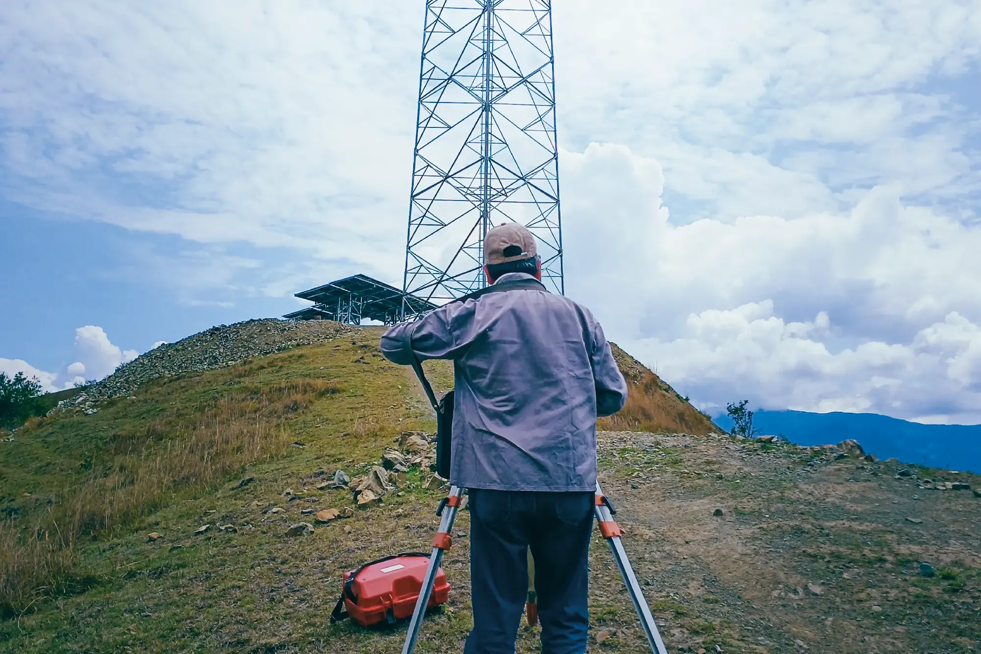 Topógrafo de TOPOCARUD realizando levantamiento topográfico frente a torre de telecomunicaciones en terreno montañoso de Colombia